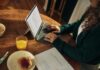 집에서 쉽게 따라하는 마인드풀 식사, 건강하게 먹는 새로운 습관 Woman typing on laptop at wooden table with breakfast.