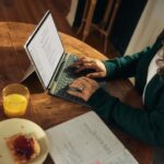 집에서 쉽게 따라하는 마인드풀 식사, 건강하게 먹는 새로운 습관 Woman typing on laptop at wooden table with breakfast.
